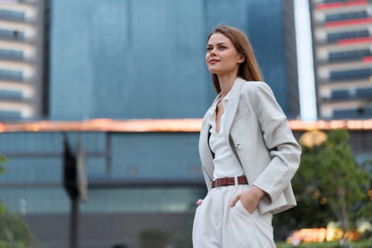 confident woman in white business suit walking outdoors in urban environment with modern glass buildings and natural evening light, expressing empowerment and professionalism in business concept
