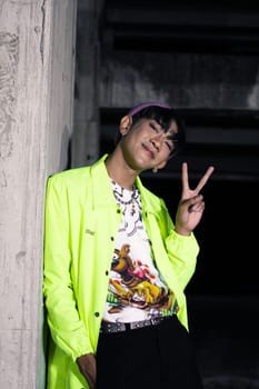 an asian man in a lime colored jacket leaning against a disused building pillar looking very handsome at night