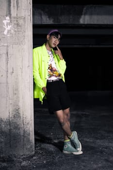 an asian man in a lime colored jacket leaning against a disused building pillar looking very handsome at night