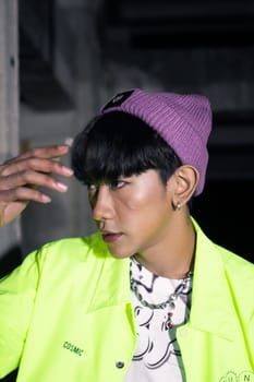 an asian man in a lime colored jacket leaning against a disused building pillar looking very handsome at night