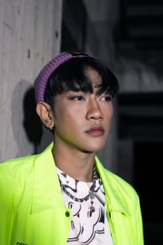 an asian man in a lime colored jacket leaning against a disused building pillar looking very handsome at night