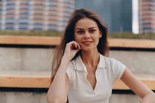 Smiling young woman wearing a white polo shirt poses outdoors with an urban background, radiating confidence and natural beauty, captured in warm summer light.