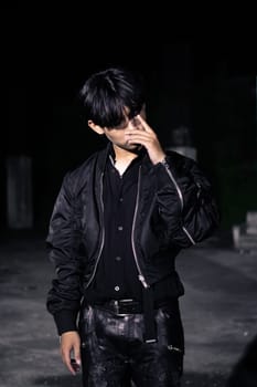 an asian man in a black parachute jacket posing very manly in a building at night