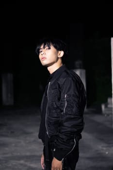 an asian man in a black parachute jacket posing very manly in a building at night