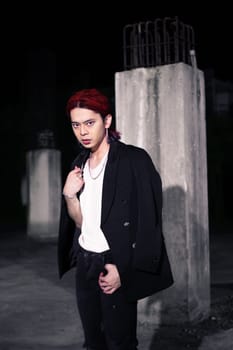 a red haired asian man wearing a white t shirt and black suit in an old building at night