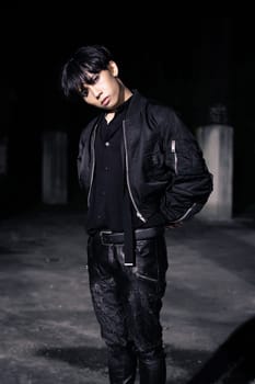 an asian man in a black parachute jacket posing very manly in a building at night