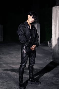 an asian man in a black parachute jacket posing very manly in a building at night