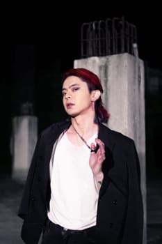 a red haired asian man wearing a white t shirt and black suit in an old building at night