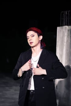 a red haired asian man wearing a white t shirt and black suit in an old building at night