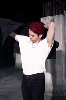 a red haired asian man wearing a white t shirt and black suit in an old building at night