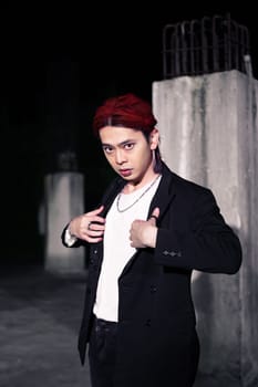 a red haired asian man wearing a white t shirt and black suit in an old building at night