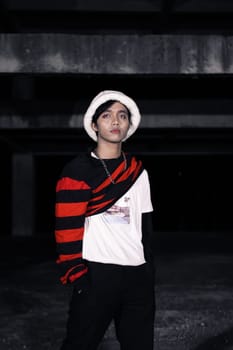 an Asian man with a striped red shirt and a chain necklace around his neck in an old building