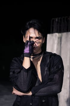an Asian man dressed all in black and black hair posing as masculine in front of a building pillar