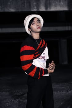 an Asian man with a striped red shirt and a chain necklace around his neck in an old building