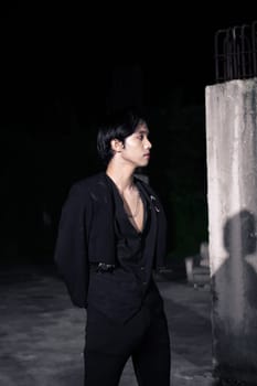 an Asian man is standing in black clothes and wearing makeup at night