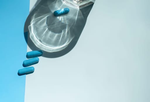 capsules of medicine on a blue background. capsules of blue color, next to a glass of water