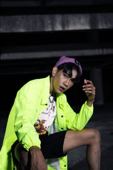 an asian man in a green jacket posing and sitting very casually in an abandoned building