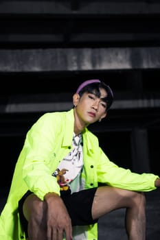 an asian man in a green jacket posing and sitting very casually in an abandoned building