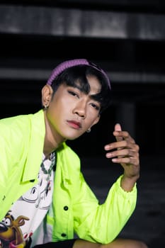 an asian man in a green jacket posing and sitting very casually in an abandoned building