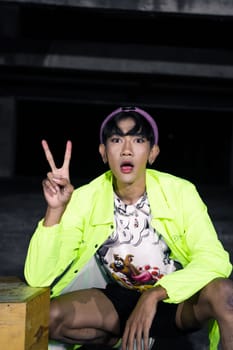 an asian man in a green jacket posing and sitting very casually in an abandoned building