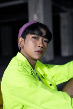an asian man in a green jacket posing and sitting very casually in an abandoned building