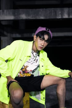 an asian man in a green jacket posing and sitting very casually in an abandoned building