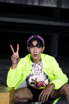 an asian man in a green jacket posing and sitting very casually in an abandoned building
