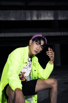 an asian man in a green jacket posing and sitting very casually in an abandoned building