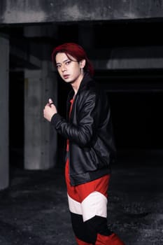 an asian man with red hair and a black jacket is posing in an abandoned building at night