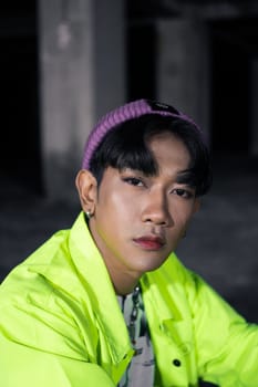 an asian man in a green jacket posing and sitting very casually in an abandoned building