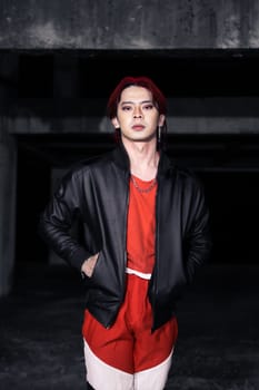 an asian man in a red shirt and earrings in his ears is standing in an abandoned building