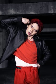an asian man in a red shirt and black jacket posing with his hands in an abandoned warehouse
