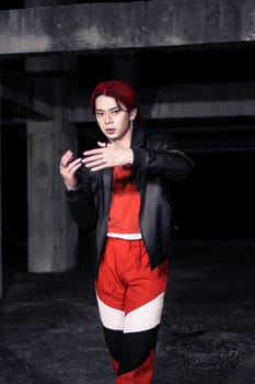 an asian man in a red shirt and black jacket posing with his hands in an abandoned warehouse