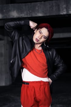 an asian man in a red shirt and black jacket posing with his hands in an abandoned warehouse