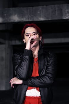 an asian man in a red shirt and black jacket posing with his hands in an abandoned warehouse