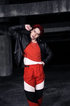 an asian man in a red shirt and black jacket posing with his hands in an abandoned warehouse