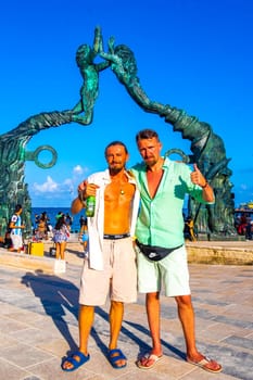 Tourists travelers friends at ancient architecture of the Portal Maya in the Fundadores park with blue sky and turquoise seascape and beach panorama in Playa del Carmen Mexico.