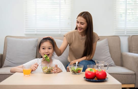 A mother gently encourages her daughter to enjoy a healthy salad during mealtime at home, fostering wellness and healthy eating habits.