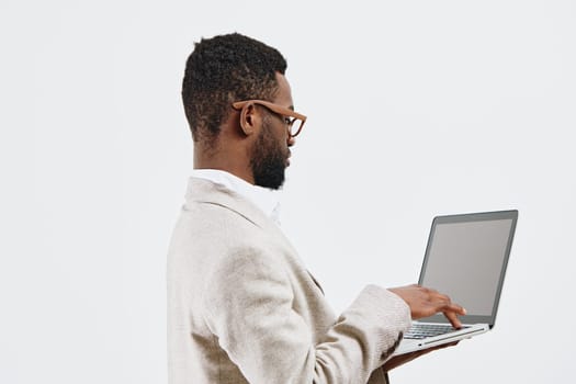 Modern professional man with curly hair and glasses working on a silver laptop in a bright, plain studio environment. Casual attire, technology use, productivity, contemporary lifestyle, minimal background.