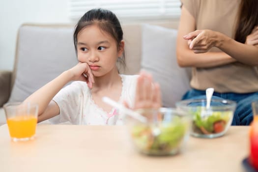 A girl shows resistance to eating her healthy salad while her mother reacts, highlighting the emotional boundaries in promoting wellness.