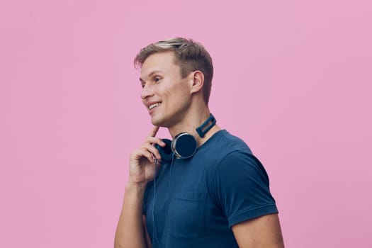 Happy young man with headphones casually dressed, smiling and looking to the side, pink studio background, relaxed mood, portrait photography, everyday life concept, bright color palette.