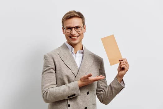 Smiling caucasian man holding envelope in hand wear glasses and beige jacket isolated on white background. Man presenting mail or message concept in digital communication and remote work scenarios. Concept: digital communication