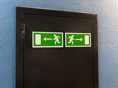 Minimalist composition with two symmetrical emergency exit signs on black panel against blue wall, combining graphic clarity and functional interior detail in modern public space or institution