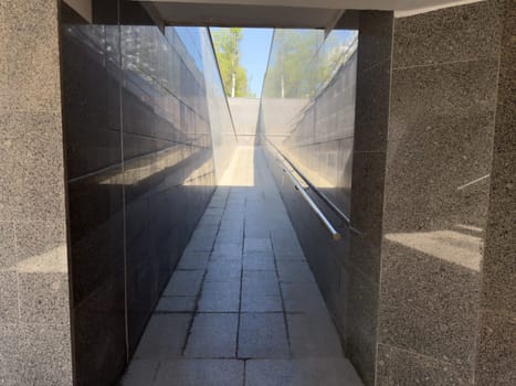 Brightly lit underground ramp with smooth stone floor and reflective granite walls leading to open sky, creating strong linear perspective and clean architectural composition in modern city passage