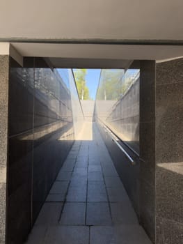 Gently inclined pedestrian ramp with smooth granite surface and handrails on both sides provides accessible pathway for wheelchairs and strollers in modern public infrastructure setting