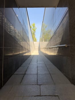 Shaded urban ramp leading toward bright blue sky, symbolizing transition and direction, with strong perspective lines and contrast between darkness and light in modern built environment