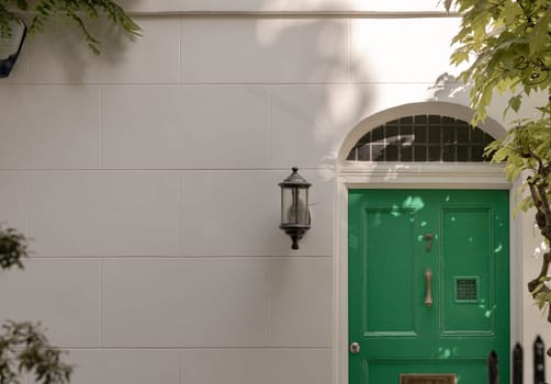 London, UK - May 08, 2025 - Green composite door is closed with Knock brass door and outdoor wall lantern on White concrete walls front of the House number 7. use it as your Wallpaper, Poster and Space for text, Selective focus.
