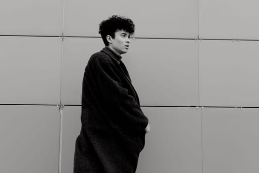 Fashion photo of a young man standing in front of a black and white wall with a gray building in the background.