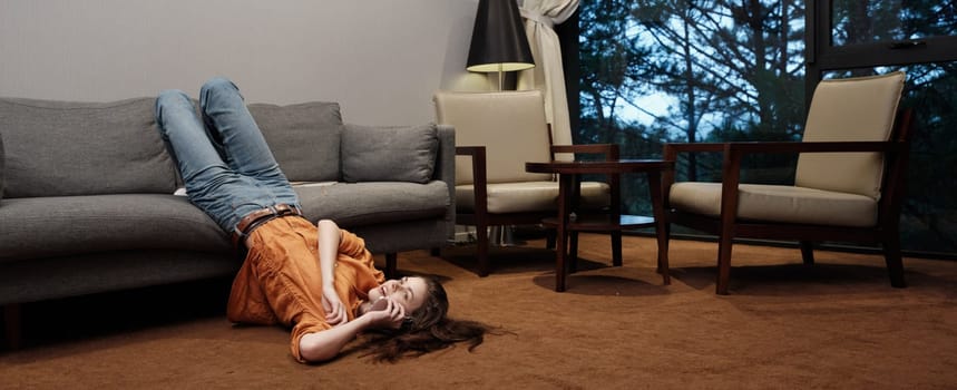 A young woman in an orange sweater and jeans reclines on a gray sofa, depicting a serene and reflective expression in a stylish living room environment