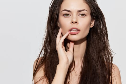 This image features a young woman with long, wet hair and minimal makeup, set against a soft gray backdrop Her expression conveys calmness and natural beauty, making it ideal for beauty and skincare concepts